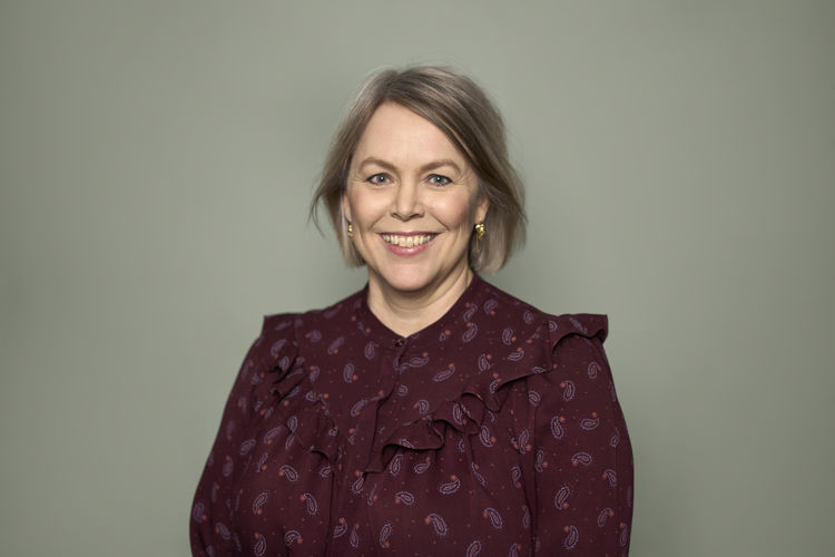 Kvinne med blondt hår og vinrød skjorte smiler til kamera.