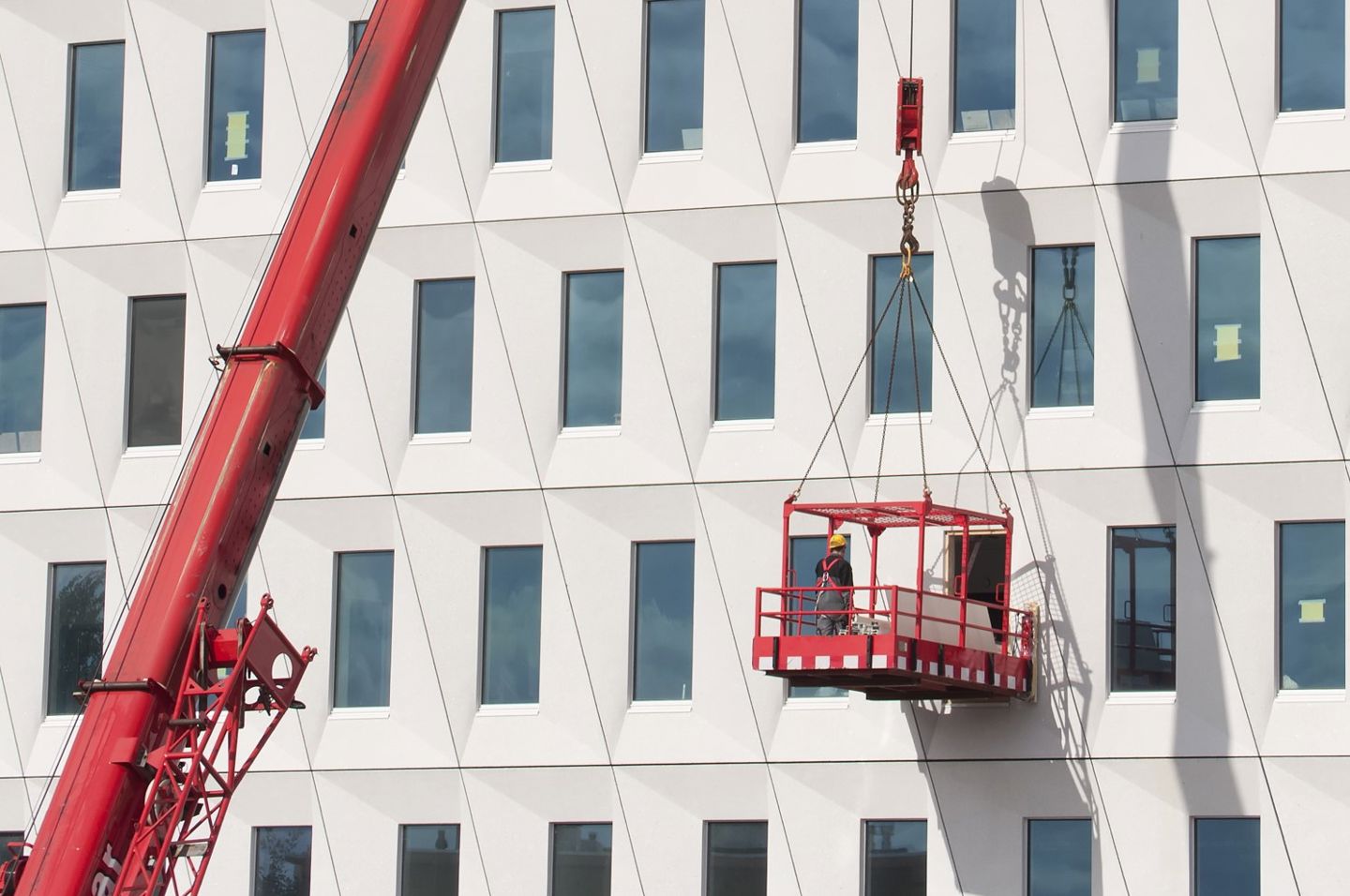 En arbeider henger i en kurv fra en kran utenfor et stort bygg