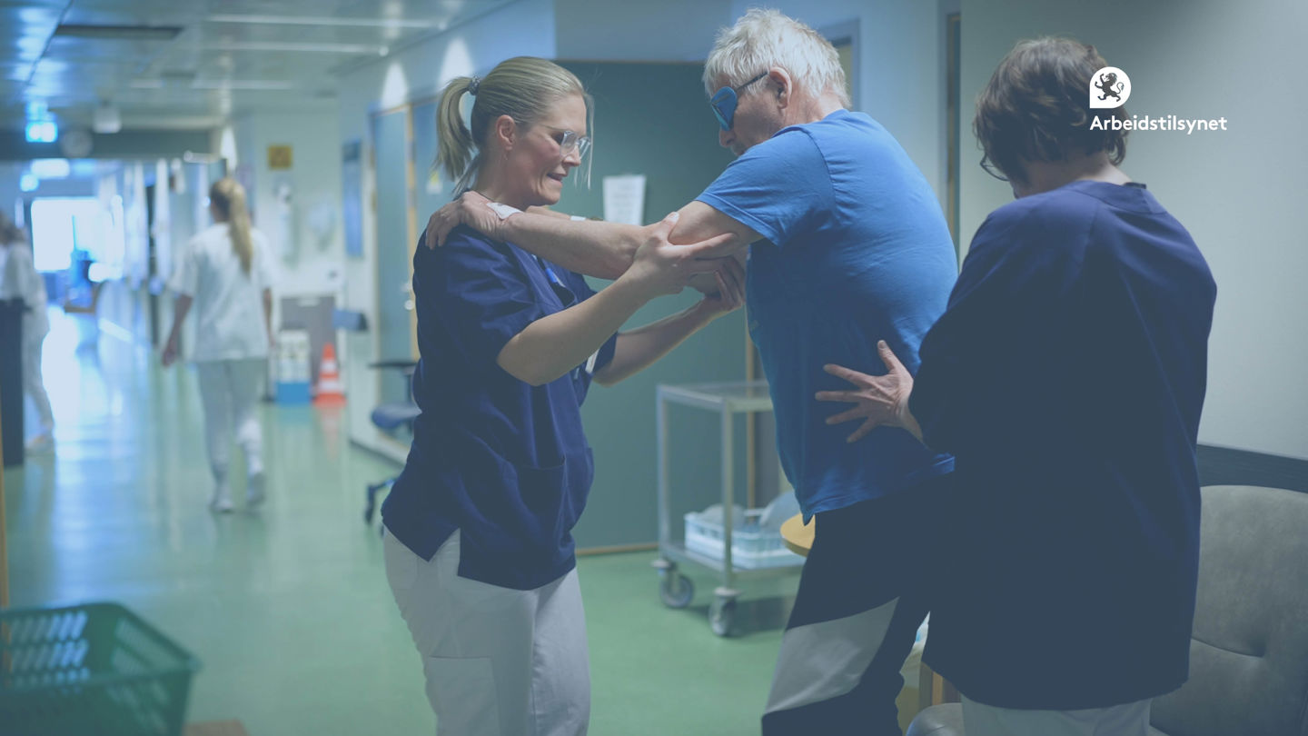 Bilde fra innslag fra et sykehus brukt i webinaret. Det er to sykepleiere og en innlagt, i en gang som gjør fysiske øvelser. Pasienten går med armene hvilende på skuldrene til sykepleier for støtte. De er vendt mot hverandre.  