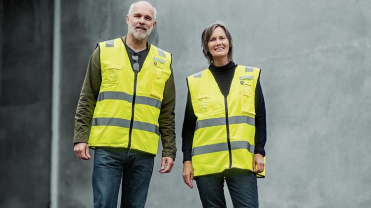 To inspektører med refleksvest, en kvinne og en mann, ser smilende inn i kamera.