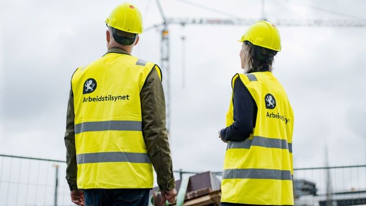 Bildet viser to personer i gule vester som står med ryggen til på en byggeplass. 